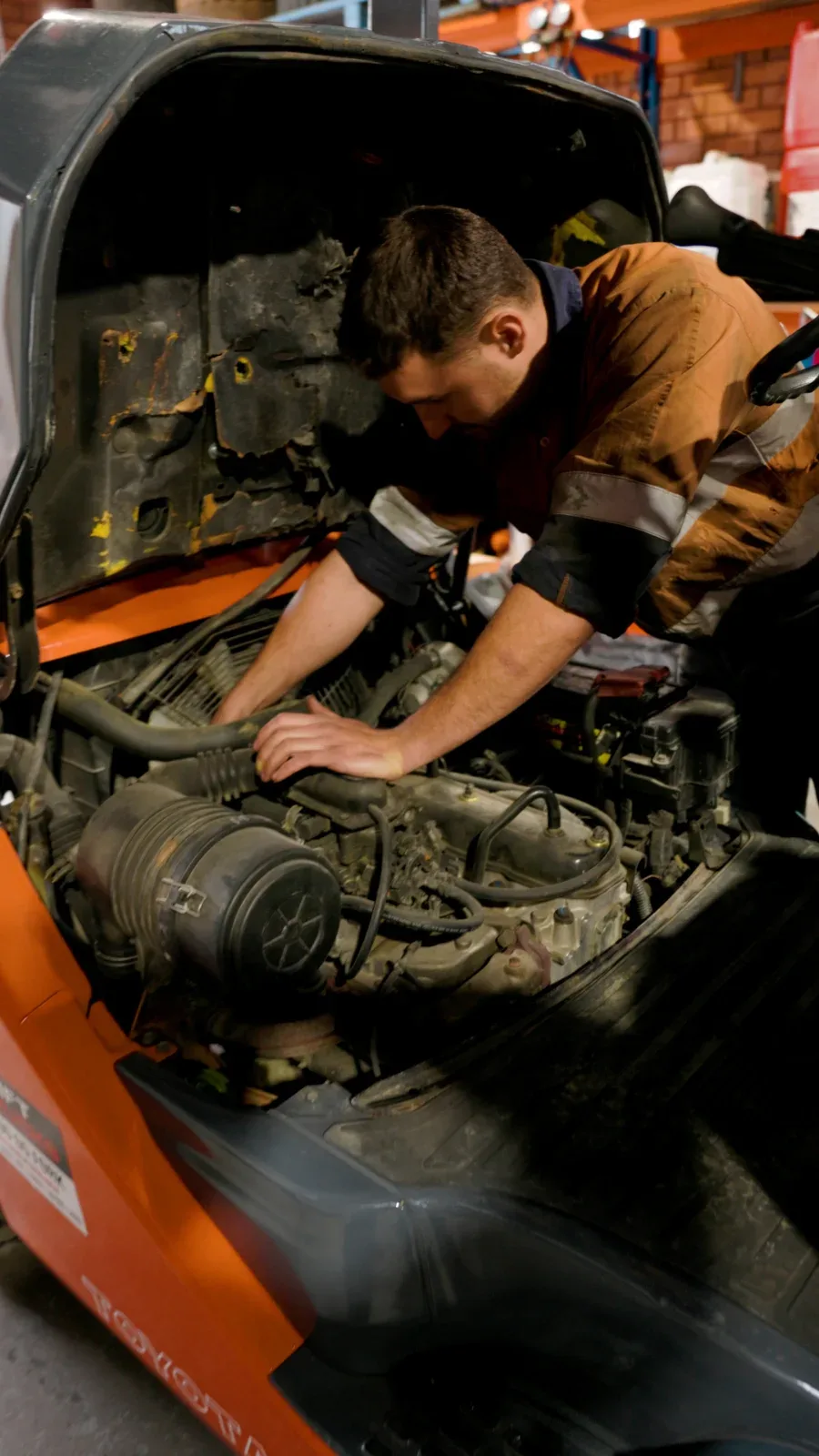 A mechanic working in the engine bay of an orange forklift