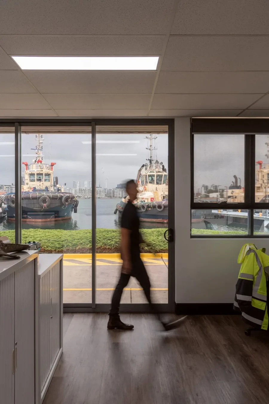 A team member walking past the office windows, tugboats moored outside