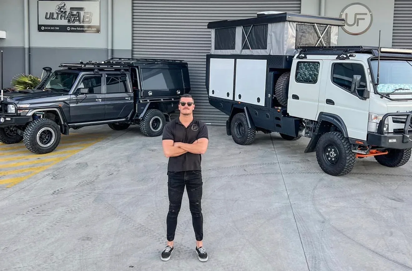 Tom from Ultra Fab standing in front of a custom troop carrier and expedition truck at the Ultra Fab workshop