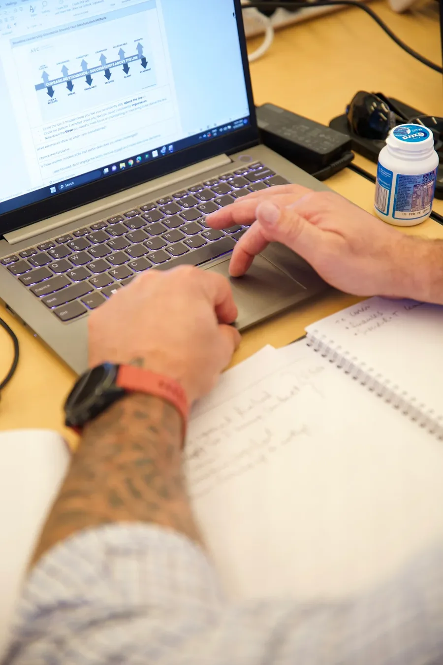 Hands on a laptop beside a notebook of handwritten notes