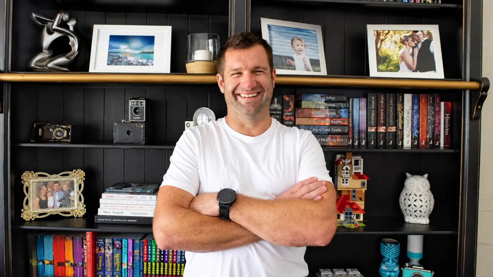 A smiling man with arms crossed in front of a bookshelf