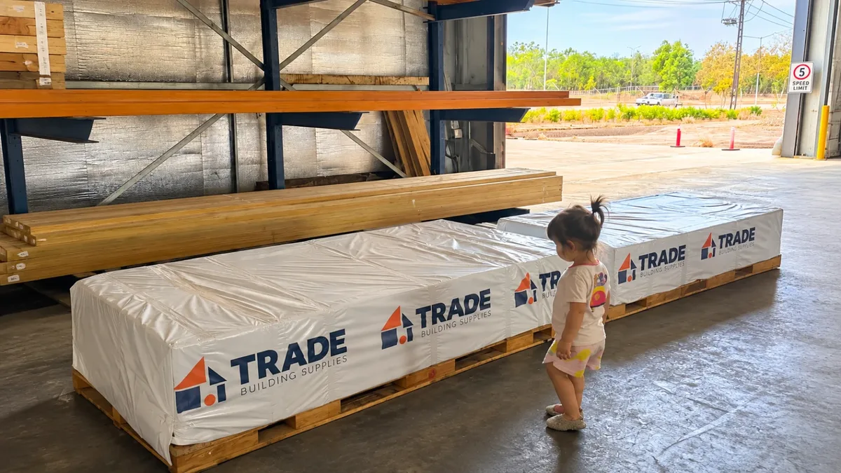 A young child beside wrapped Trade Building Supplies timber packs in the warehouse